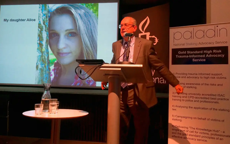 Speaker at a podium giving a talk, slide showing a photo of a woman labeled 'My daughter Alice' behind him, with a Paladin banner nearby.